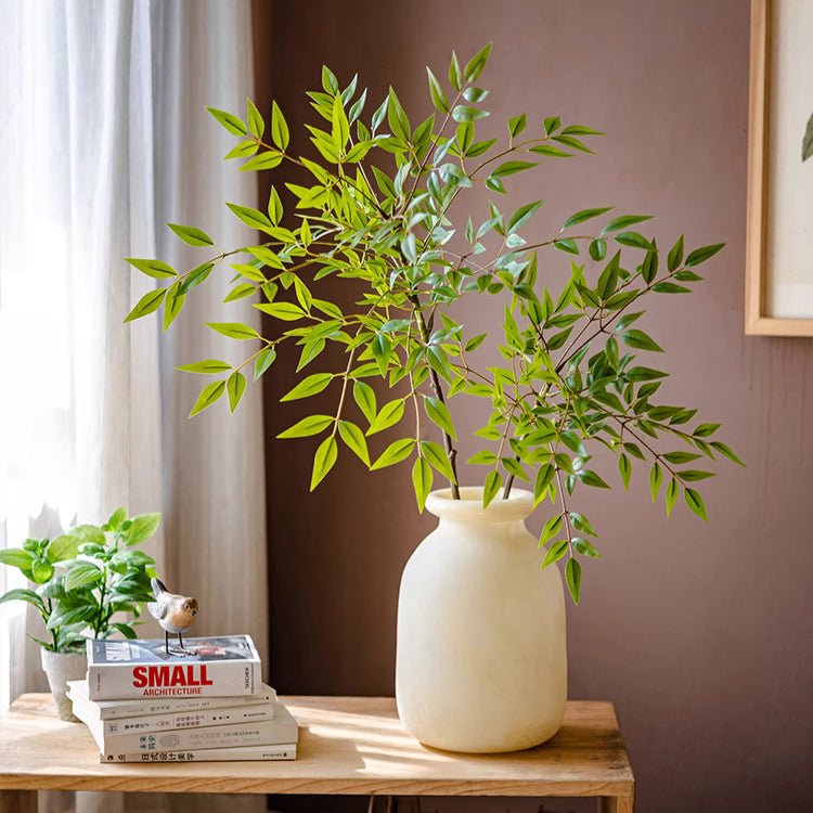White vase with green plant on a wooden table against a brown wall