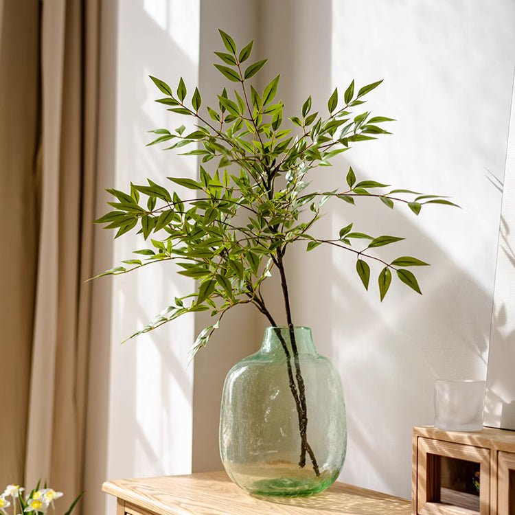 Green vase with branches on a wooden table in a bright room