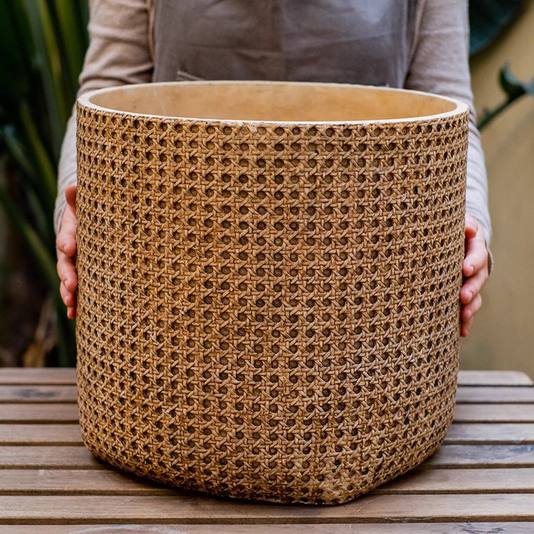 Person holding a large woven basket on a wooden surface