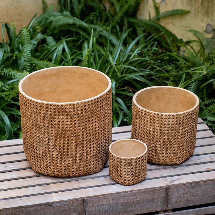 Three woven baskets of different sizes on a wooden surface with greenery in the background