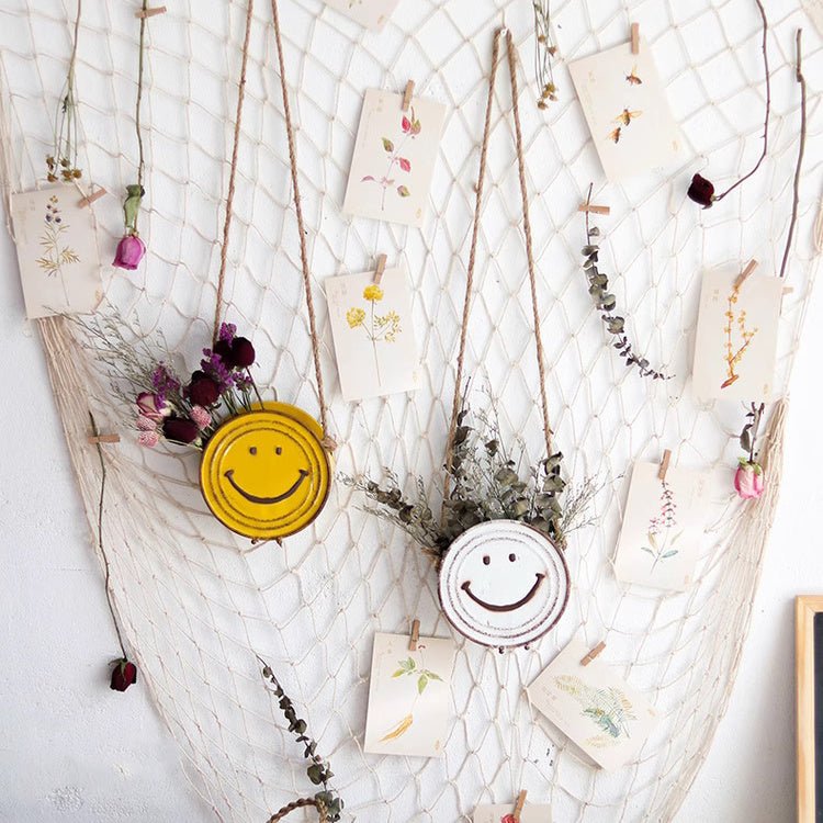 Decorative wall hanging with smiley face elements and dried plants on a textured white background
